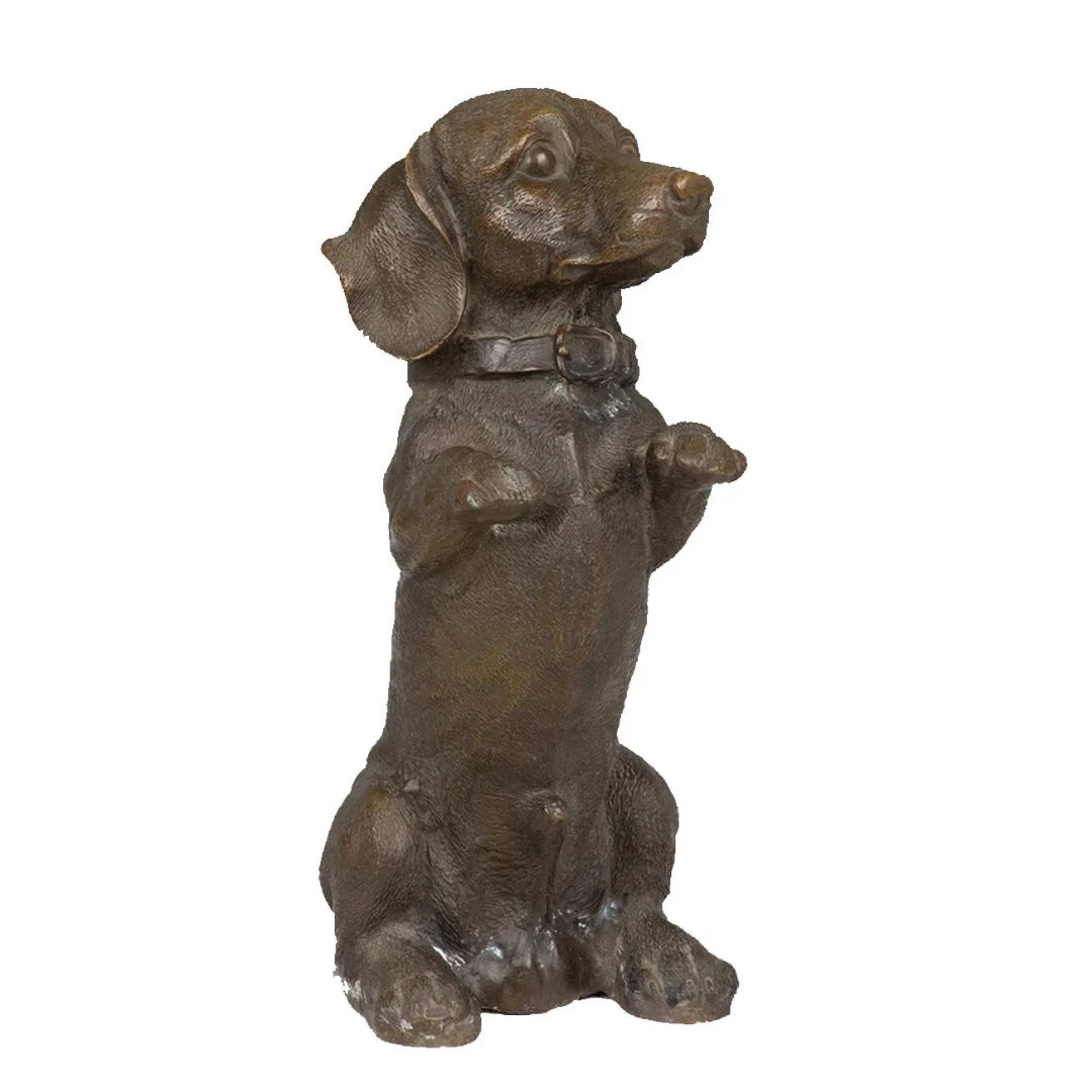 This charming bronze dachshund sculpture is crafted using the traditional lost-wax casting method, capturing the dog in a playful seated pose with its front paws raised. The warm bronze patina highlights its distinctive long body, short legs, floppy ears, and detailed collar. With an integrated bronze base for stability, this piece combines realism with whimsical character, making it a delightful accent for home decor or a thoughtful gift for dachshund lovers.