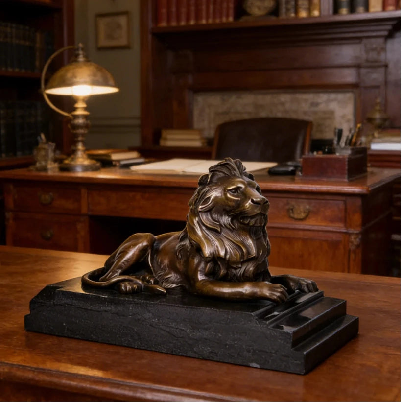 This is a majestic bronze lion sculpture, cast using the lost-wax method, depicting the animal in a poised, reclining stance. The sculpture features a rich, warm bronze patina with a smooth, polished finish that accentuates the lion’s powerful musculature and the intricate, flowing details of its mane. Its head is held high, conveying a sense of quiet authority and regal composure, while its body rests in a relaxed yet alert posture.