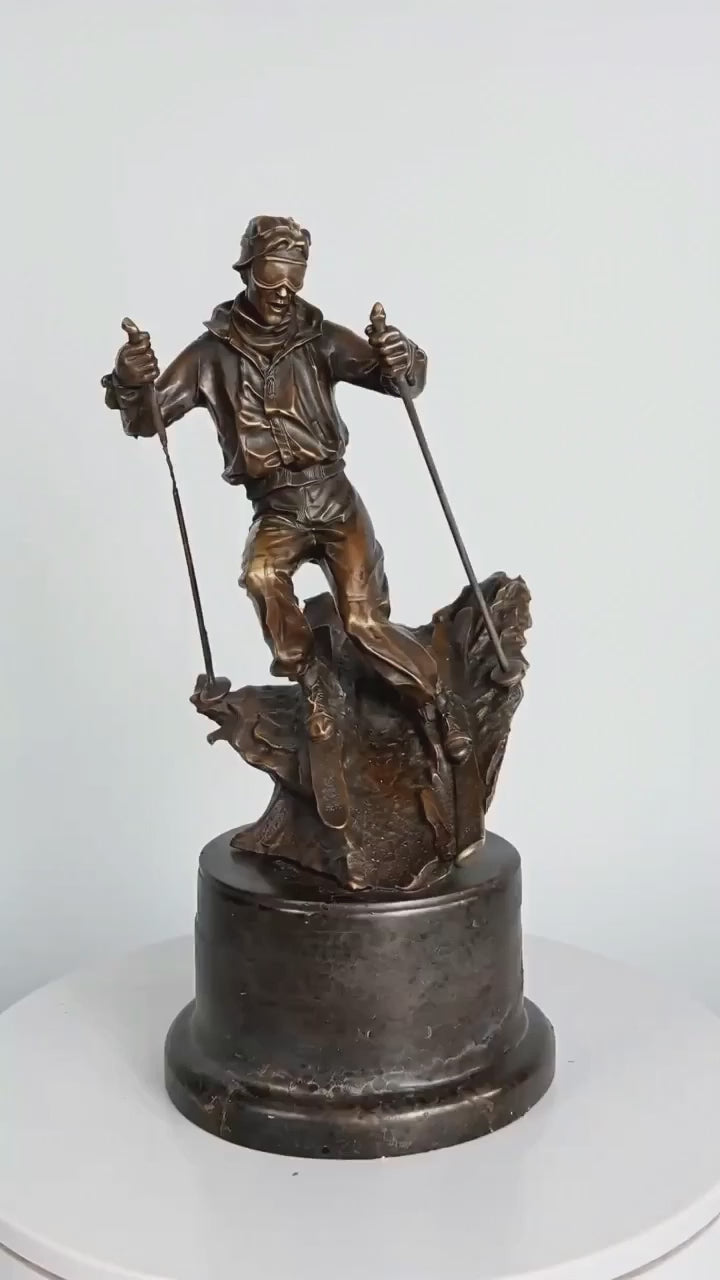 This is a dynamic bronze sculpture of a skier, crafted using the lost-wax casting method. The piece captures the athlete mid-action, navigating a rugged, snow-like terrain with ski poles firmly in hand and legs bent in a powerful stance. The rich, warm bronze patina accentuates the fluid folds of the skier’s jacket and pants, as well as the textured, naturalistic base that simulates a snow-covered slope.