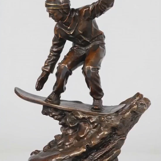 This is a dynamic bronze sculpture of a snowboarder, crafted using the lost-wax casting method. The piece captures the athlete mid-action, crouched low on their board while navigating a rugged, snow-like terrain, with one arm extended for balance. The rich, warm bronze patina accentuates the fluid folds of the snowboarder’s jacket and pants, as well as the textured, naturalistic base that simulates snowdrifts.
