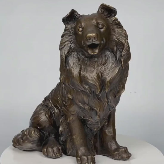 This is a lifelike bronze sculpture of a collie dog, crafted using the lost-wax casting method. The piece captures the dog in a seated pose, with its mouth open in a friendly, alert expression, conveying warmth and intelligence. The rich, warm bronze patina accentuates the intricate, flowing texture of its long, wavy coat, which cascades down its neck and body in detailed, lifelike folds.